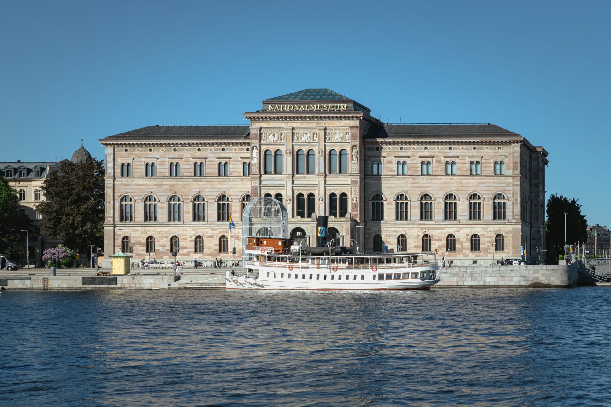 Nationalmuseums fasad speglad i vattnet med en vit ångbåt vid kajen