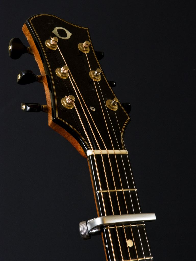 En capo fastsatt rakt över halsen på en akustisk gitarr, strax bakom andra bandet