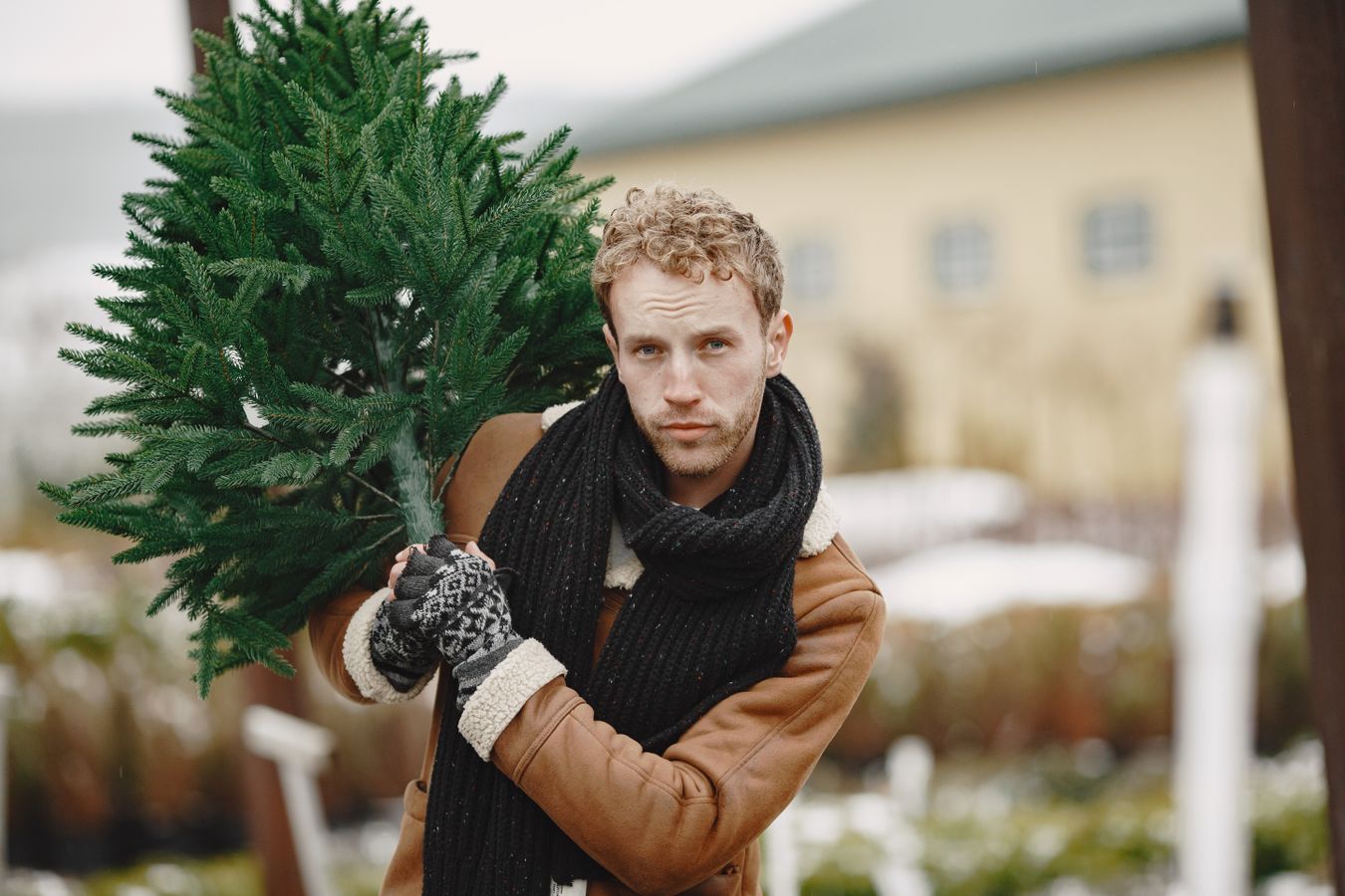 En man bär en avsågad julgran över axeln på en granförsäljning i snö
