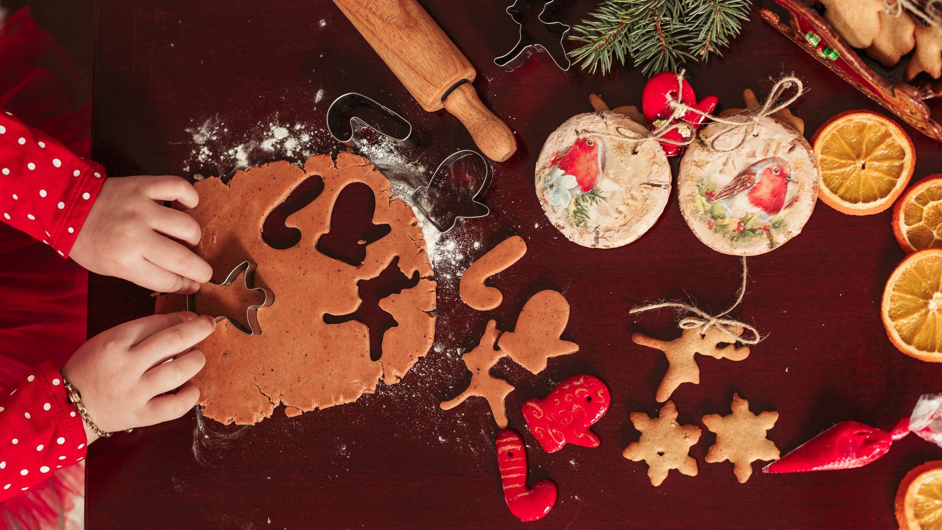 Barnhänder stansar ut pepparkaksfigurer ur deg bredvid färdiga hängande julgransdekorationer