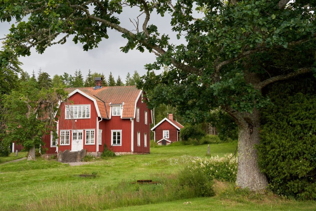 Faluröd svensk villa med vita knutar i ett sommargrönt landskap