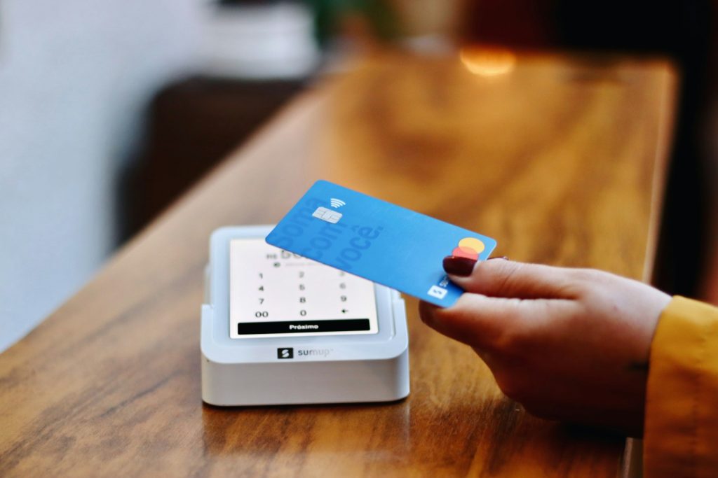 Hand som håller ett betalkort mot en kortterminal på en träbardisk
