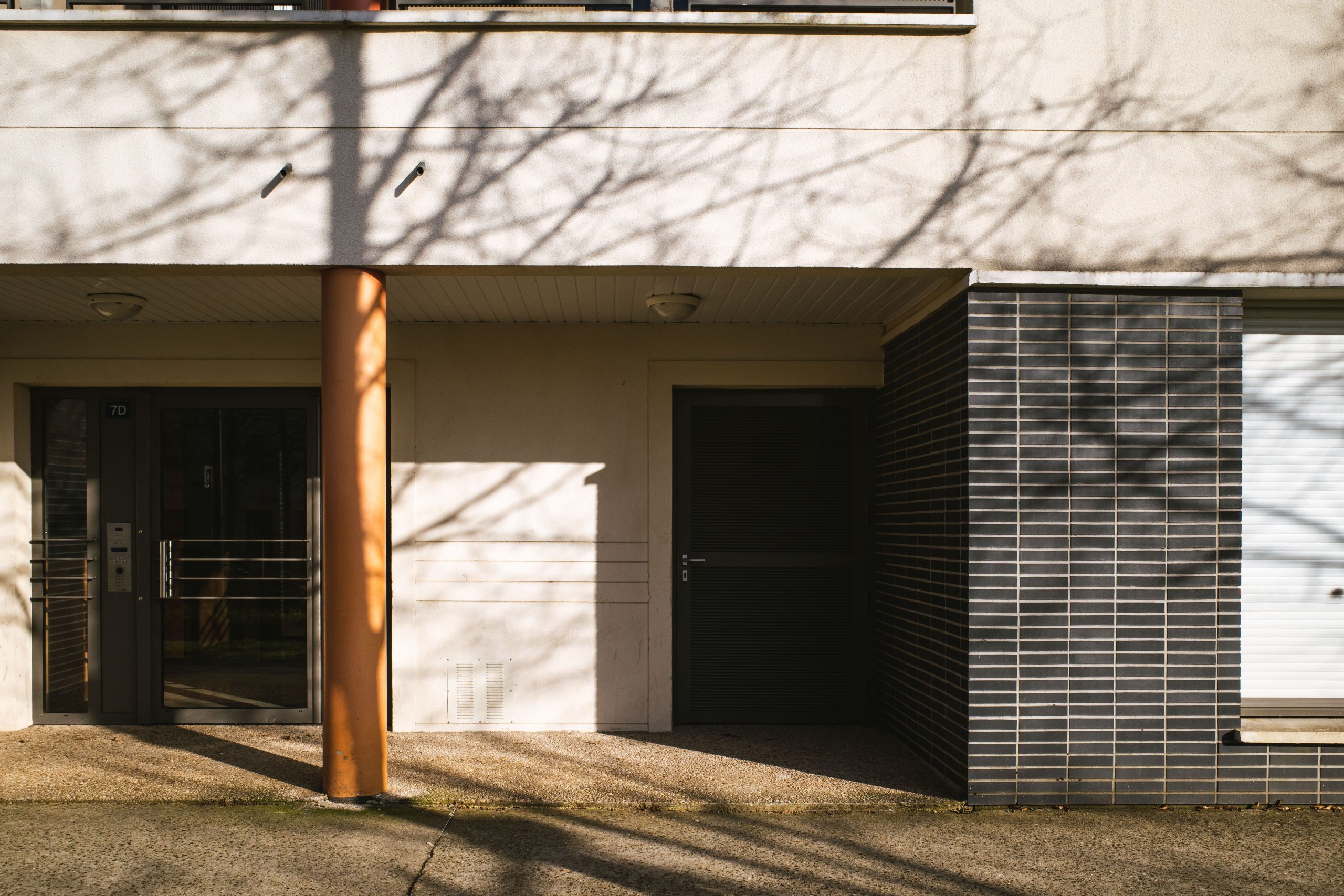 Entré till ett modernt flerbostadshus med glasad portdörr i skarpt eftermiddagsljus