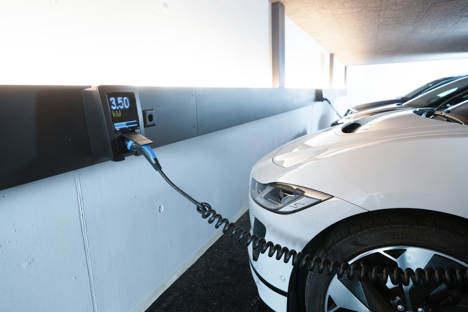 Vit elbil som laddar från en väggmonterad laddbox i ett garage
