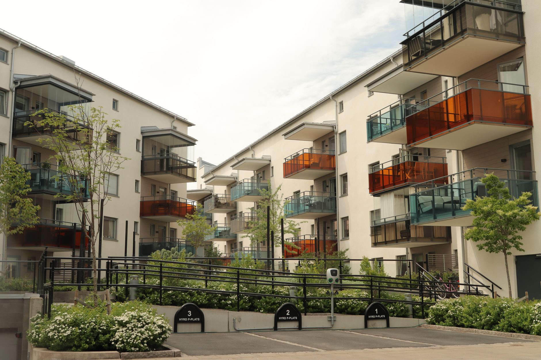 Flerbostadshus med färgade balkonger och numrerade hyrda parkeringsplatser framför