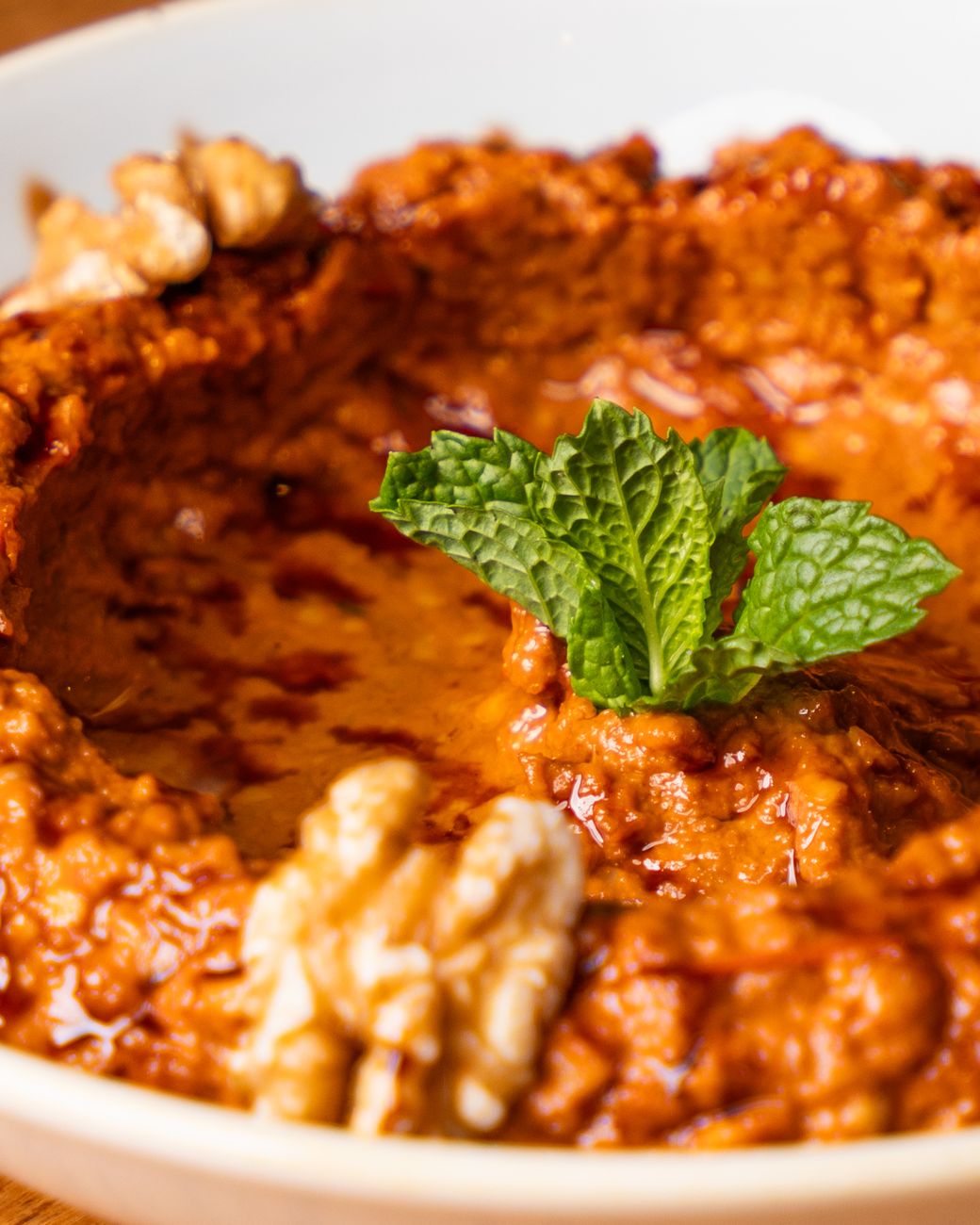 Muhammara i en vit skål, garnerad med mynta och valnötter