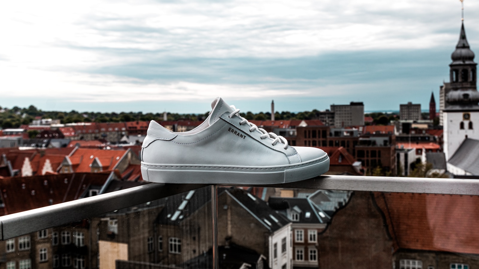 Vit klassisk lädersneaker på ett räcke med stadssiluett i bakgrunden