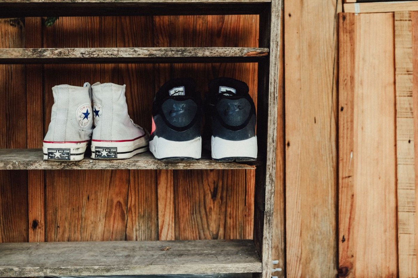 Slitna vintage-Converse och gamla Nike-sneakers på en rustik trähylla