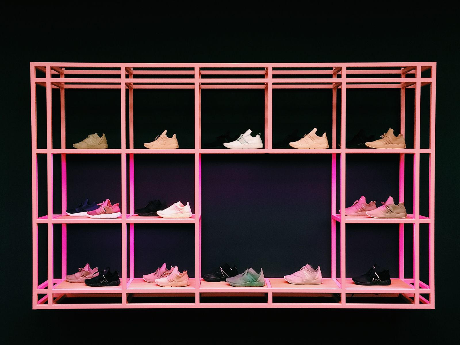 Sneakers uppstallda i par pa en rosa butikshylla mot mork bakgrund