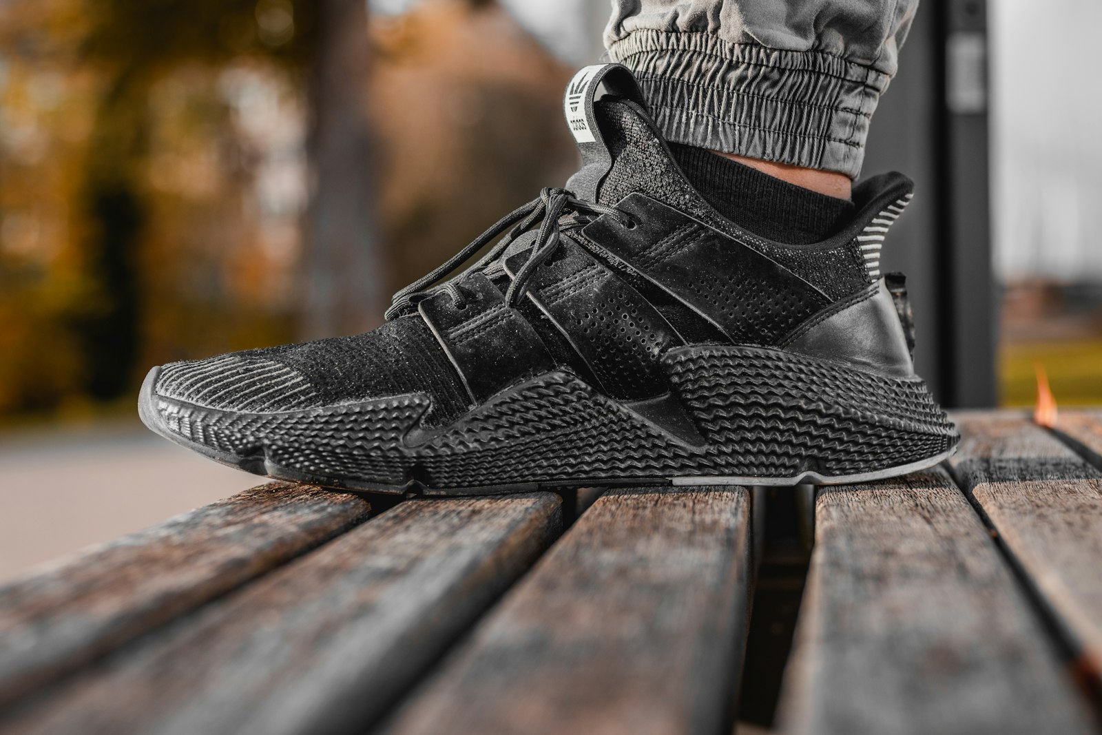Helsvart sneaker med svart sula på en träbänk i höstmiljö