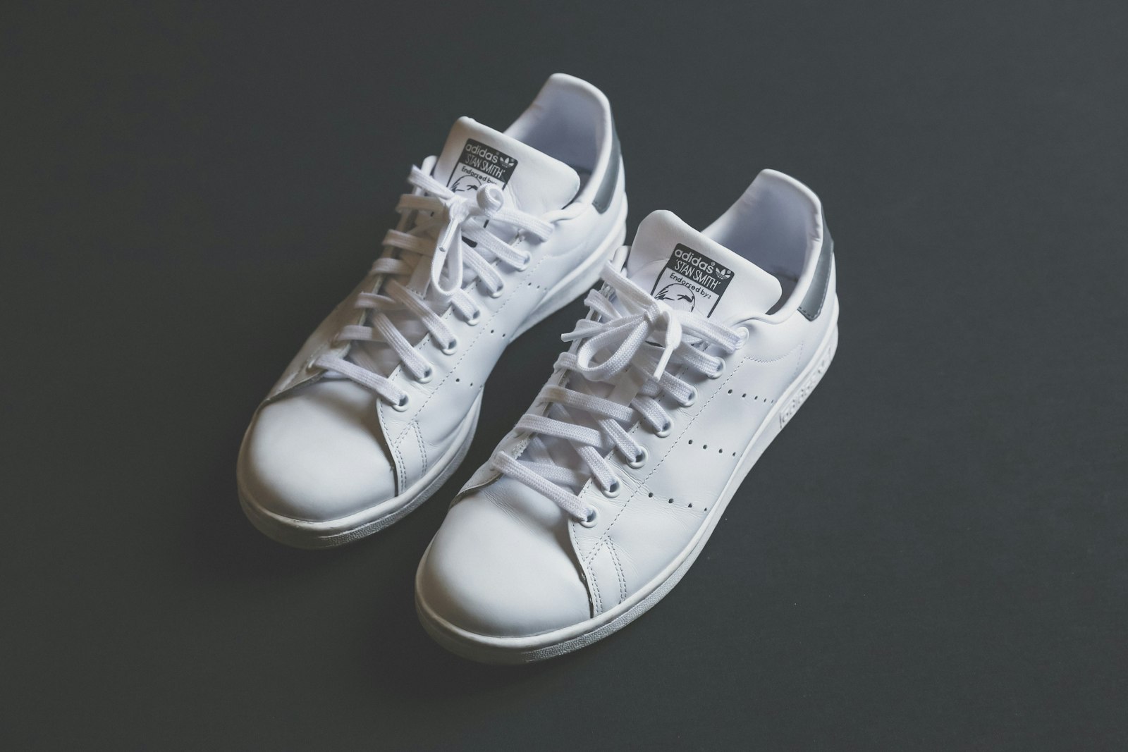 Ett par rena vita lädersneakers av modellen Adidas Stan Smith mot mörk bakgrund