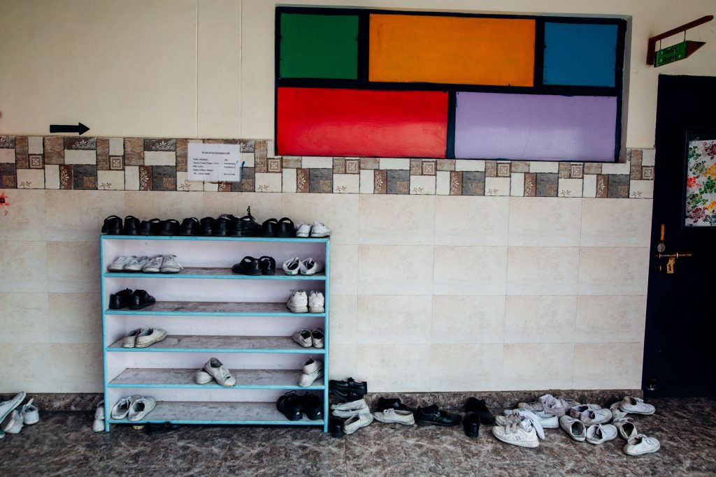 Skohylla i en skolkorridor med rader av barnskor och fler skor på golvet