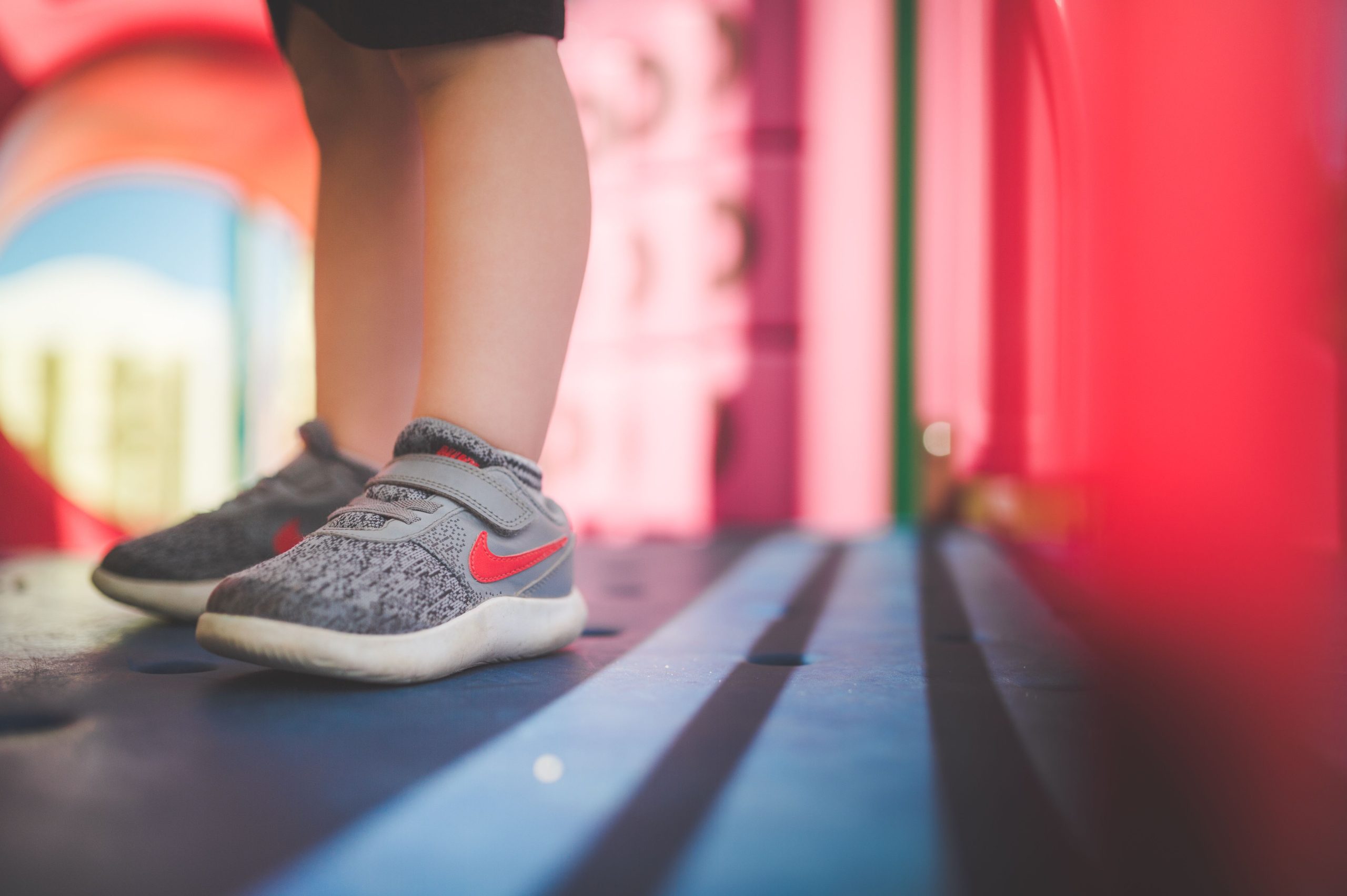 Närbild på ett barns fötter i grå sneakers med kardborreband på en lekplats