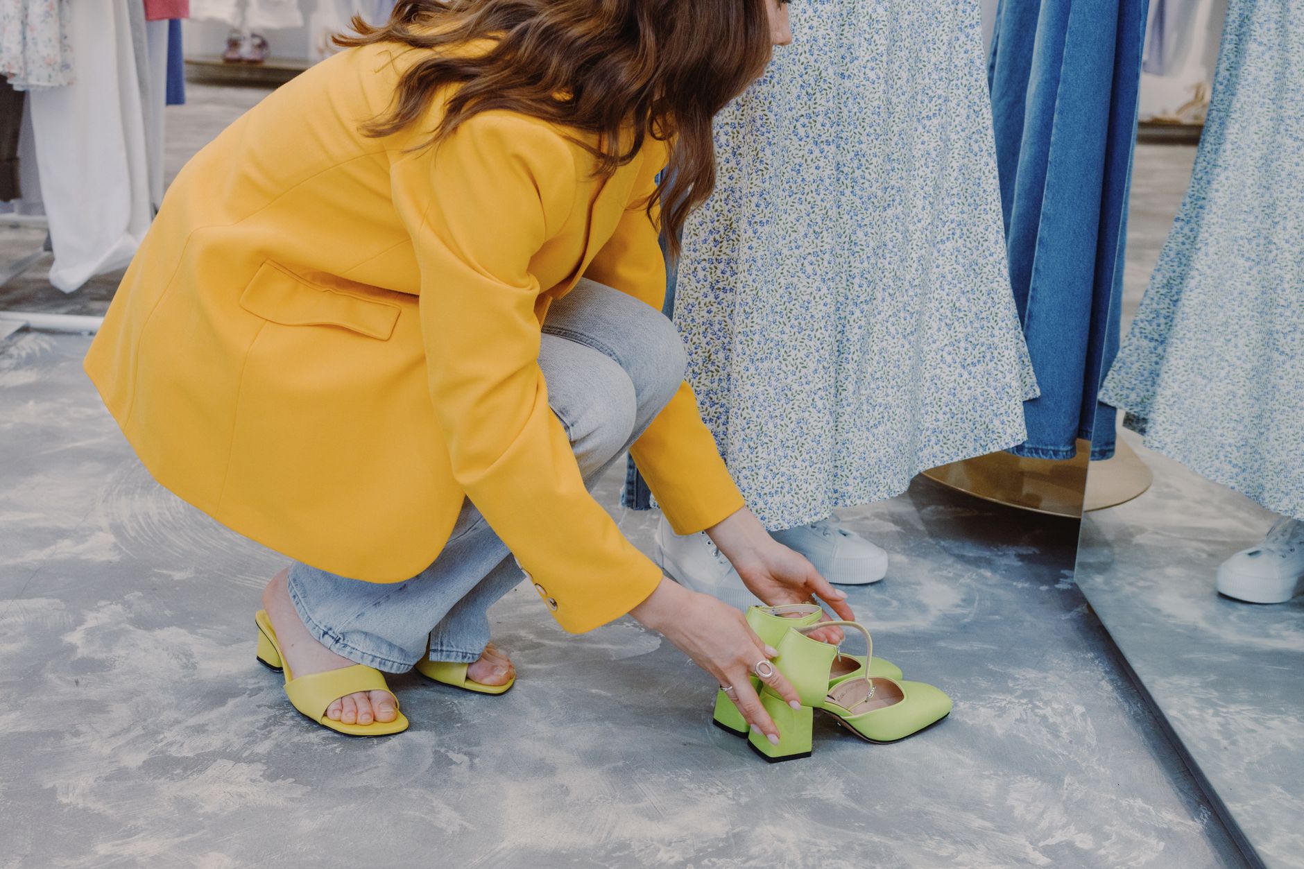 Kvinna på huk i en butik som provar ut ett par limegröna skor med blockklack.