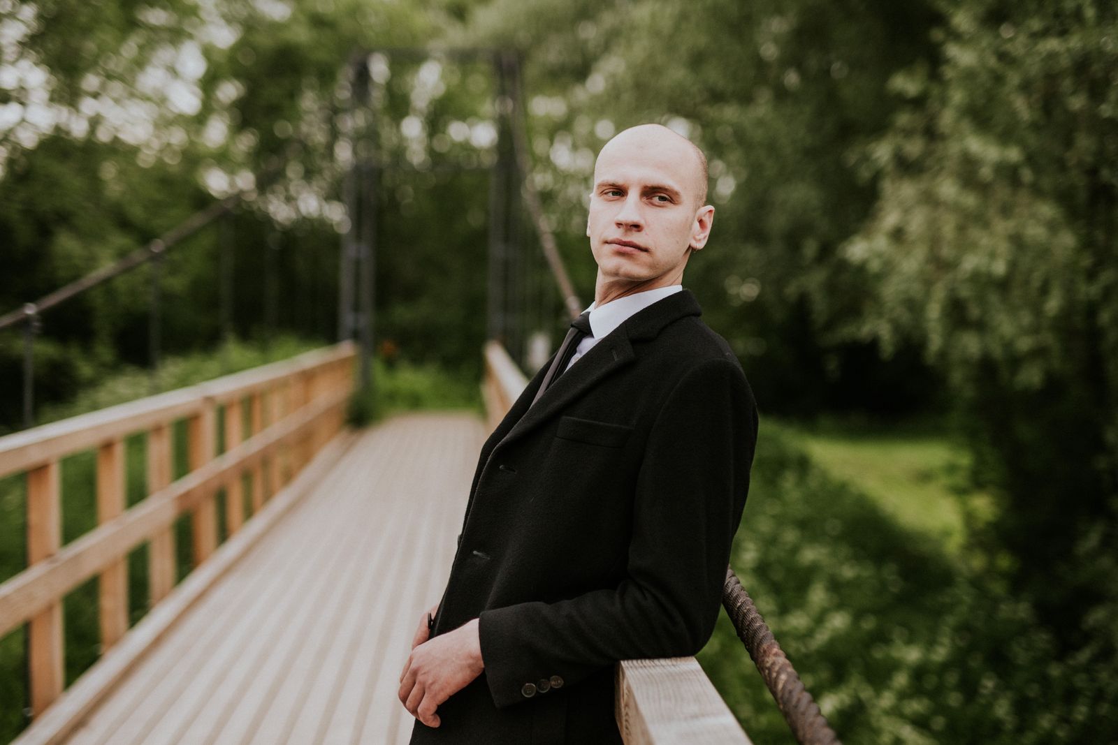 Man i svart kostym med slips på en träbro