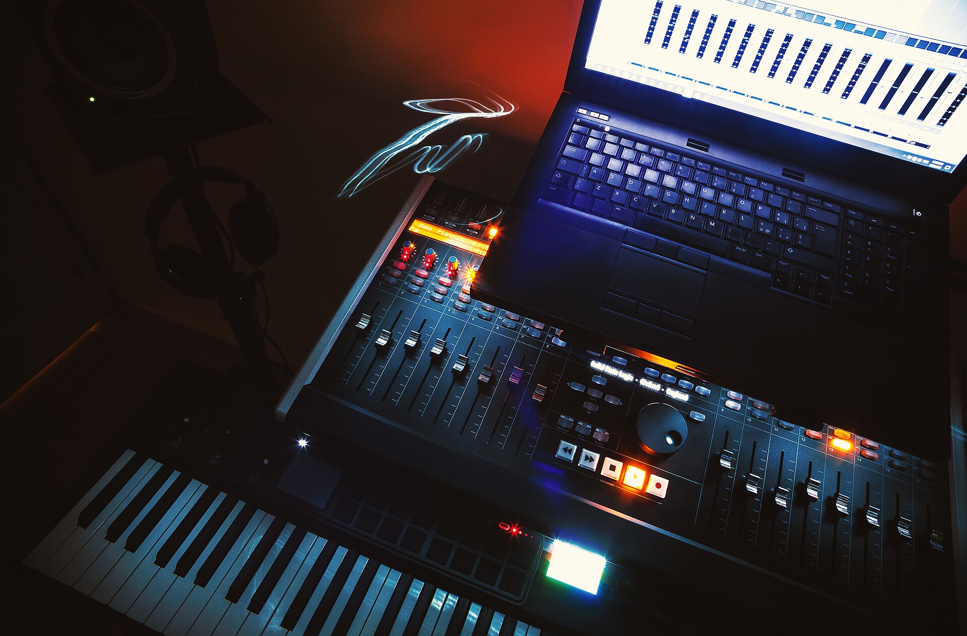 Home studio desk with a control surface, laptop running a DAW and a MIDI keyboard
