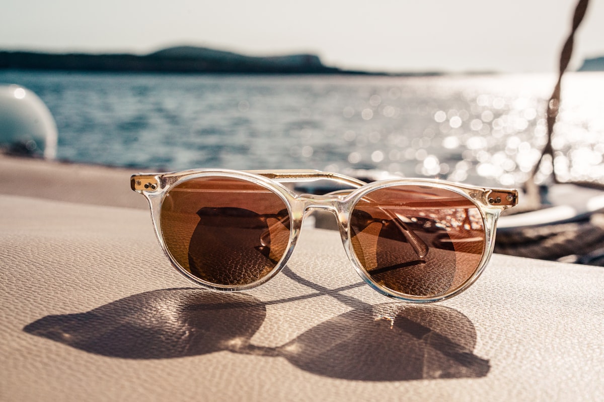 Ett par solglasögon med genomskinlig båge ligger i solljus med havet i bakgrunden