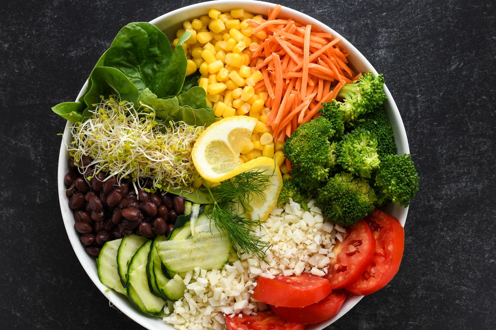 Färgglad vegansk salladsskål med spenat, majs, morot, broccoli, bönor, gurka och tomat sedd ovanifrån