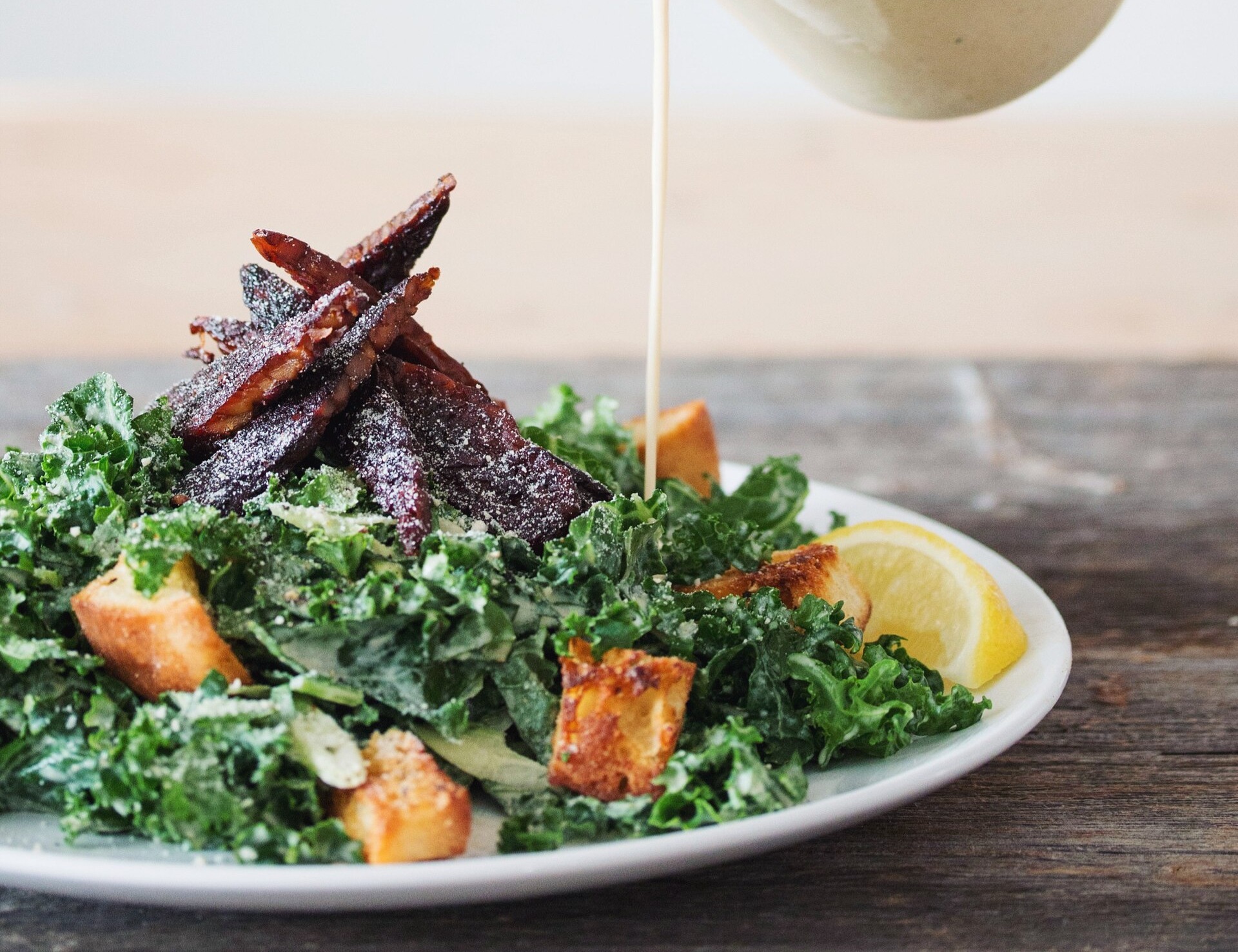 Vegansk caesarsallad med grönkål, krutonger, tempehstrimlor och krämig dressing som hälls över