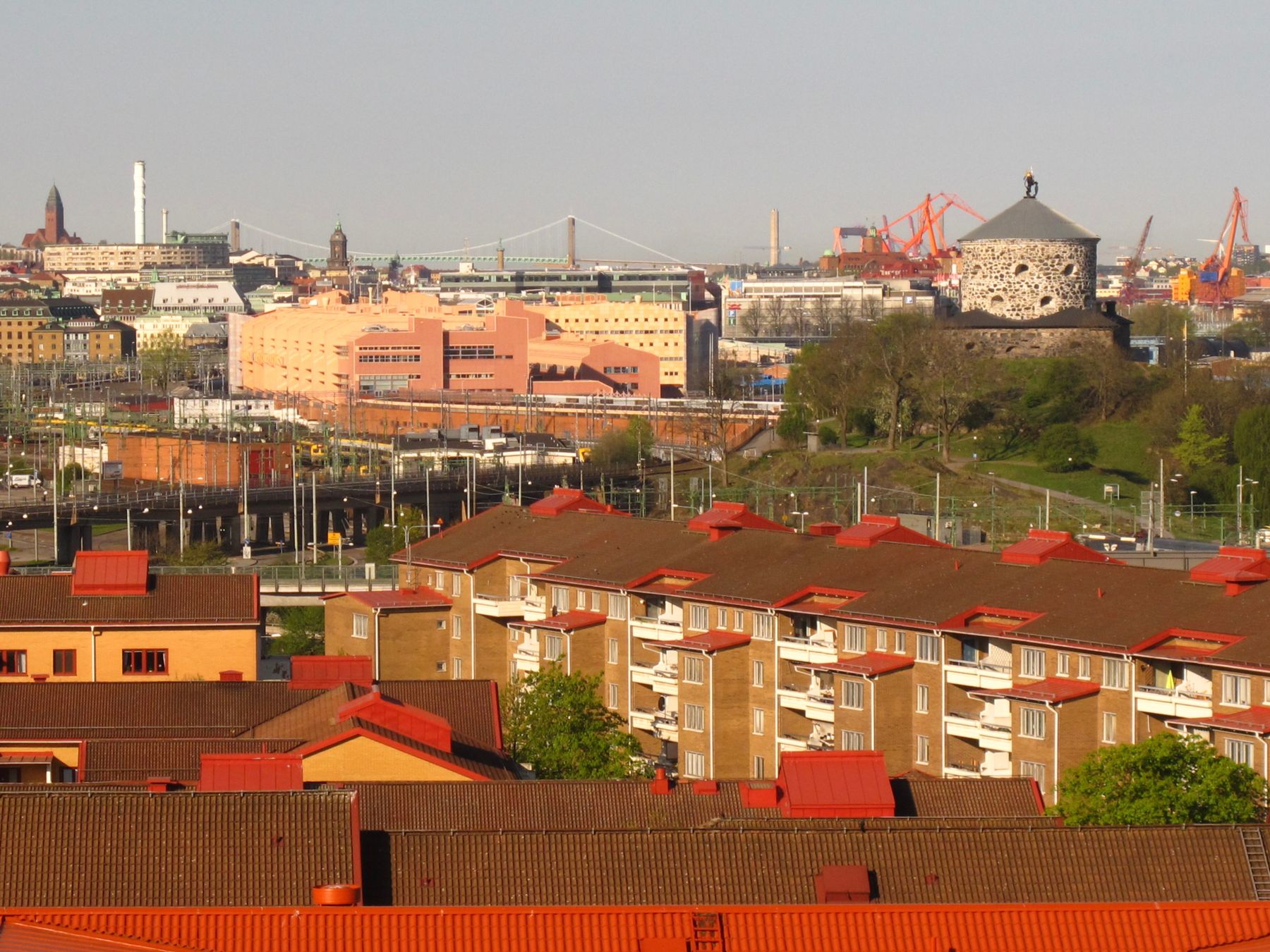Röda tak över bostadskvarter i Göteborg med en gammal skans på en höjd och hamnen i bakgrunden