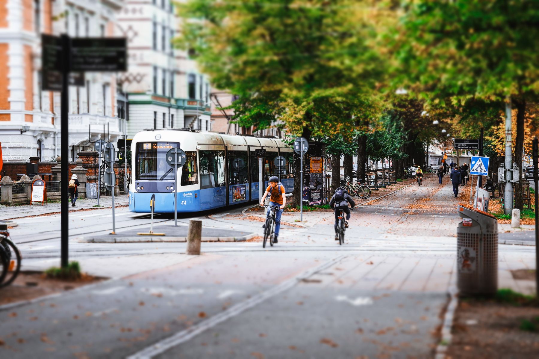 Blå spårvagn och två cyklister på en trädkantad gata i Göteborg