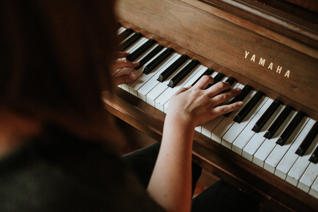 Person spelar på ett brunt piano sett över axeln