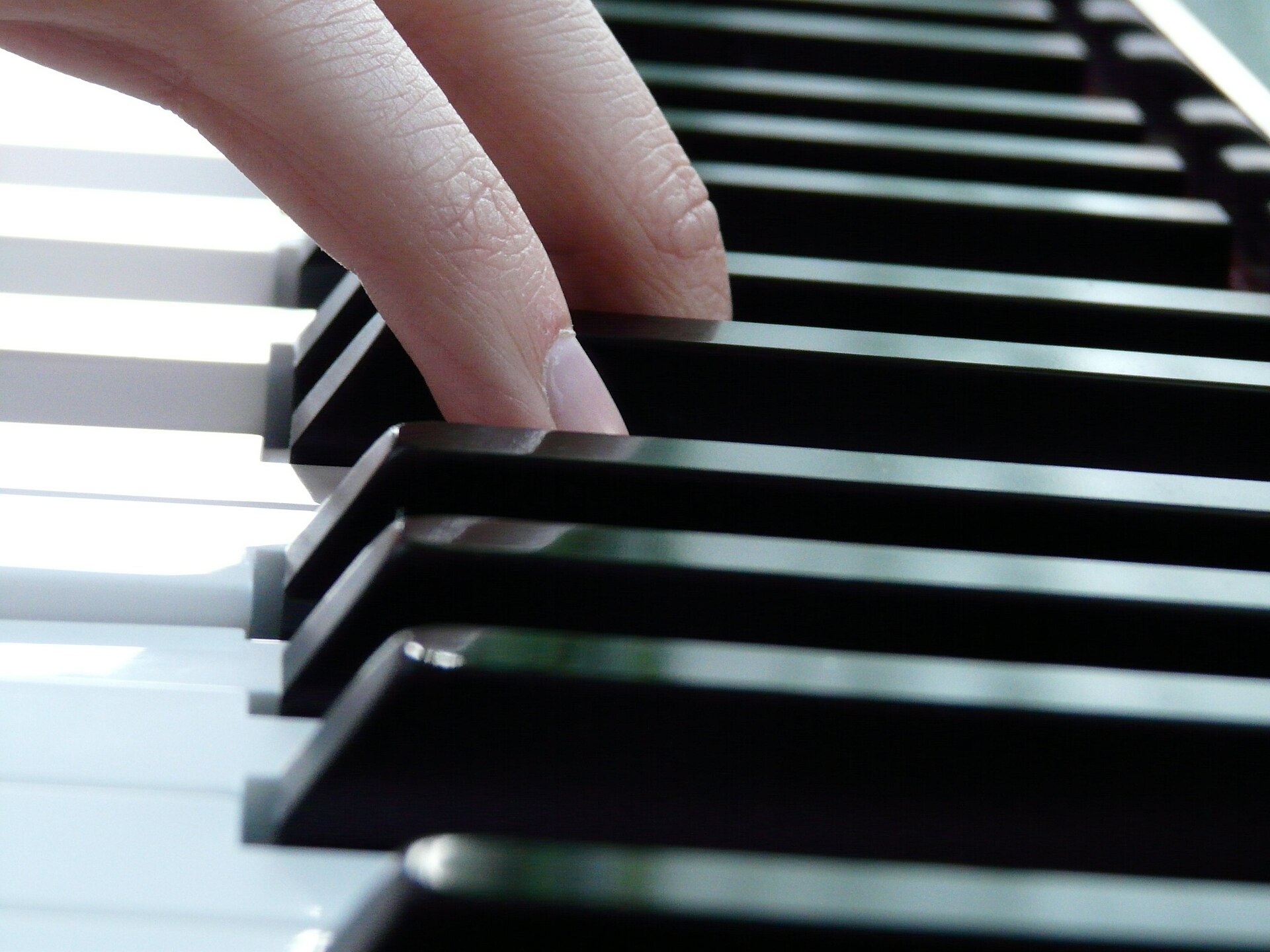 Två fingrar på svarta tangenter, sett i närbild längs ett pianos tangentbord