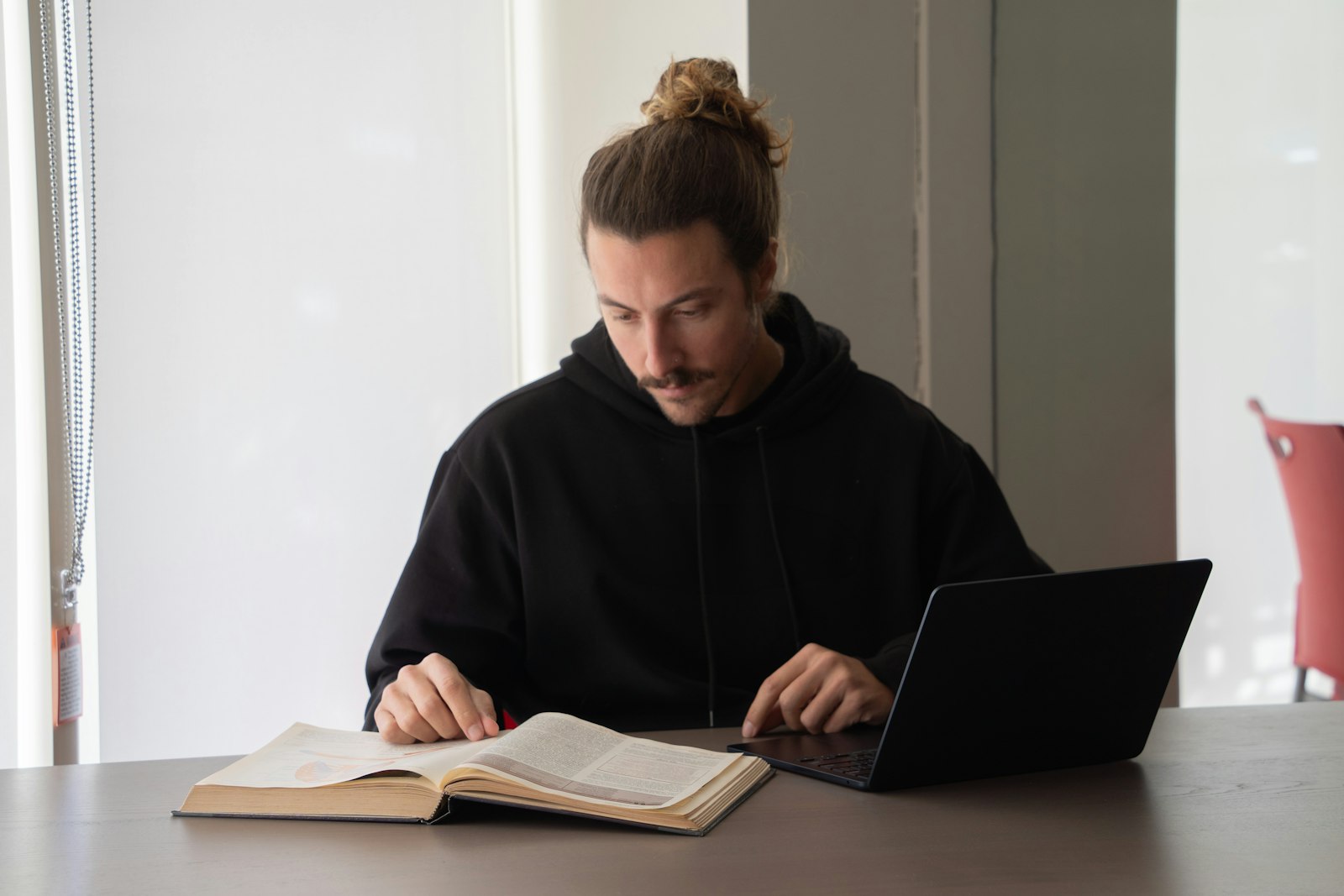 Person pluggar med bok och laptop vid ett bord