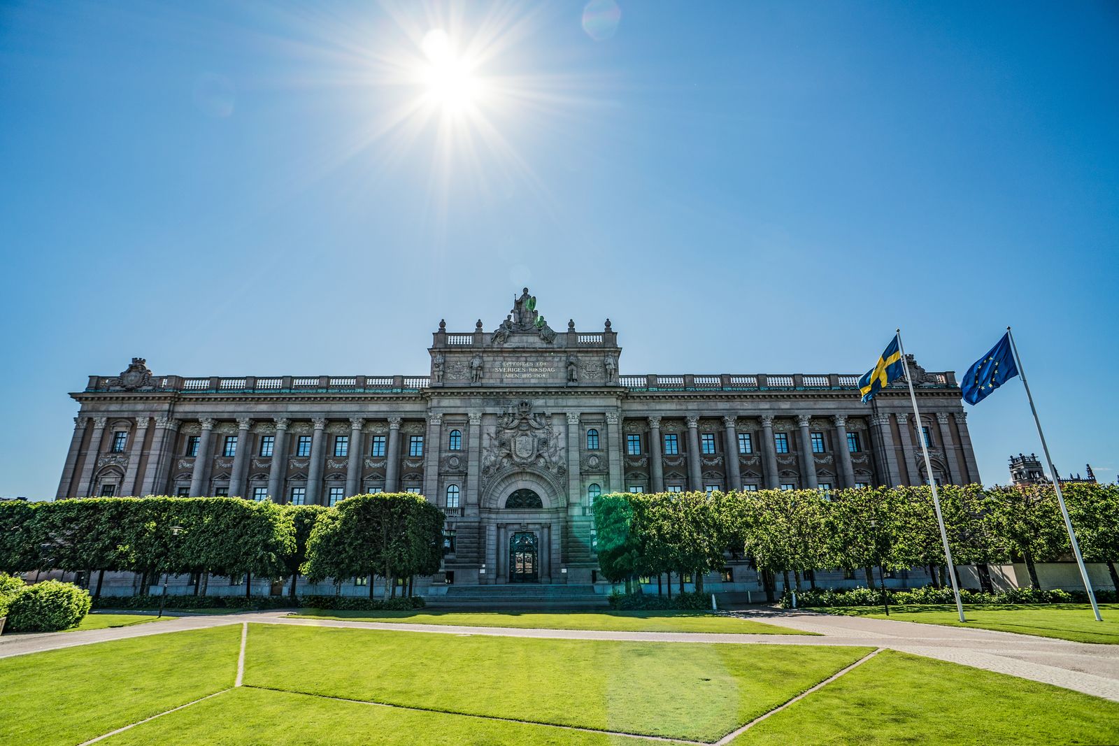Sveriges riksdagshus i Stockholm med svensk flagga och EU-flagga en solig dag