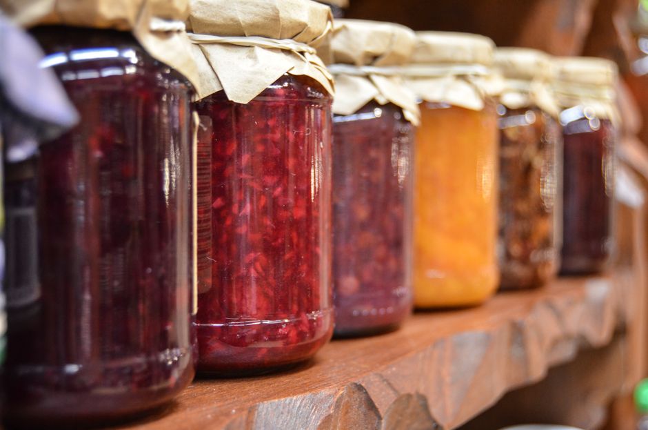 Rad med glasburkar med olika sorters sylt och marmelad på en trähylla