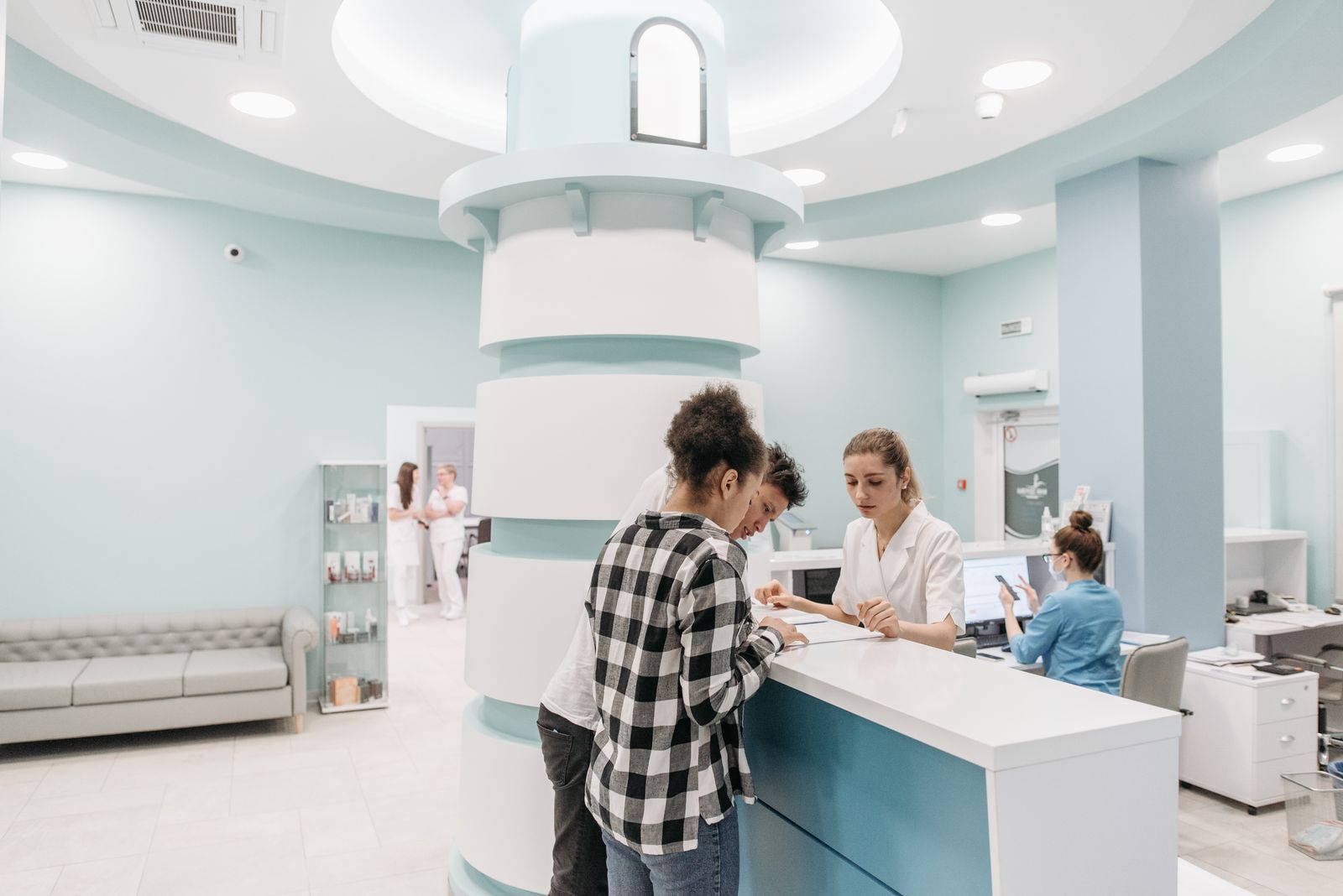 Patient fyller i uppgifter vid receptionsdisken på en vårdmottagning medan personalen hjälper till