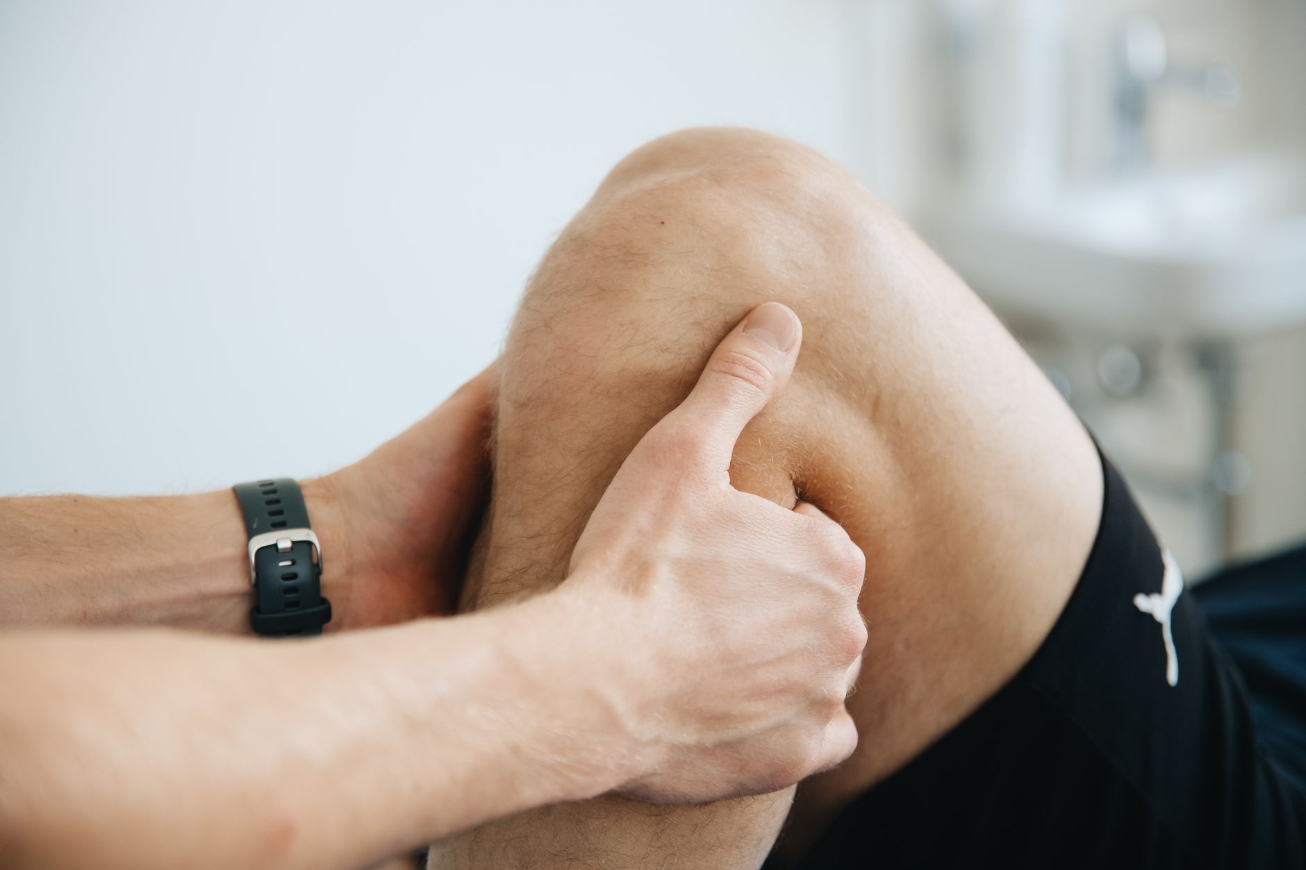 Behandlare undersöker en patients böjda knä med tummen på en ljus mottagning