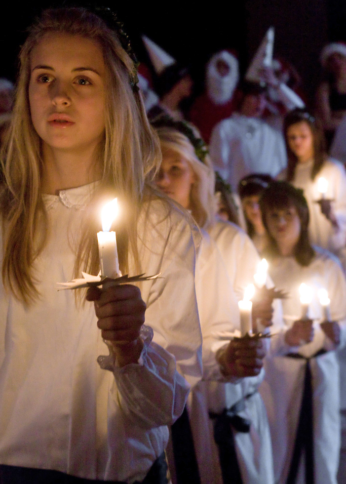 Luciatåg med vitklädd lucia och tärnor som bär levande ljus