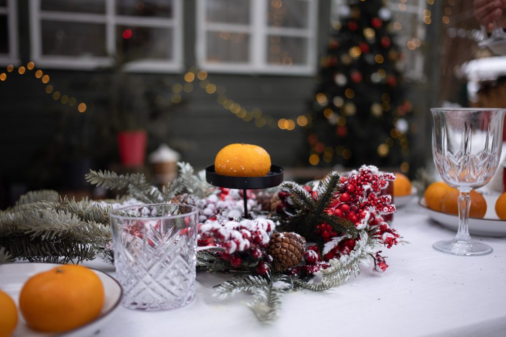 Juldukat bord med vit duk, lågt arrangemang av granris, röda bär och kottar, kristallglas och klementiner