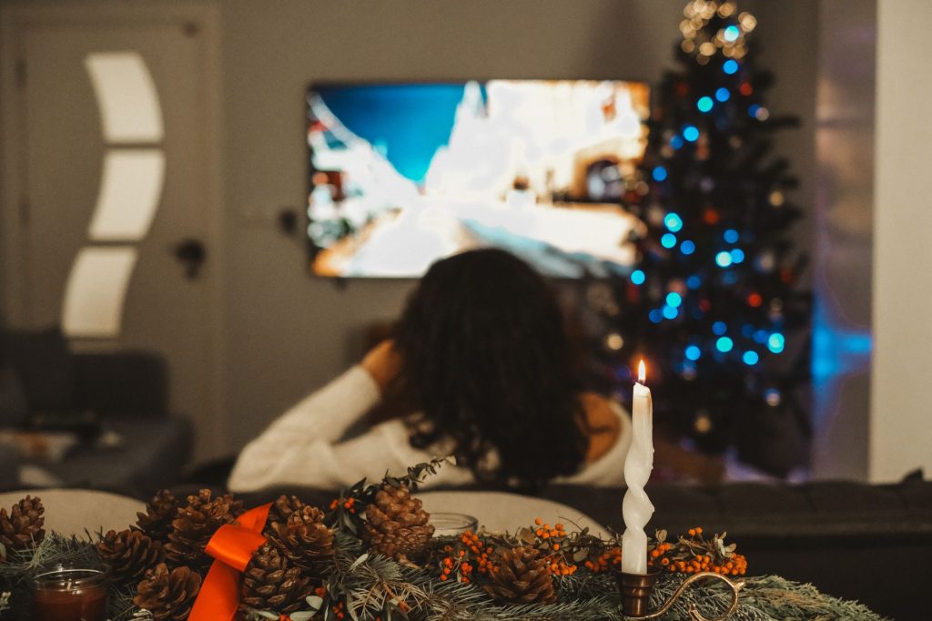 Kvinna tittar på tv vid julgranen med tänt ljus i förgrunden