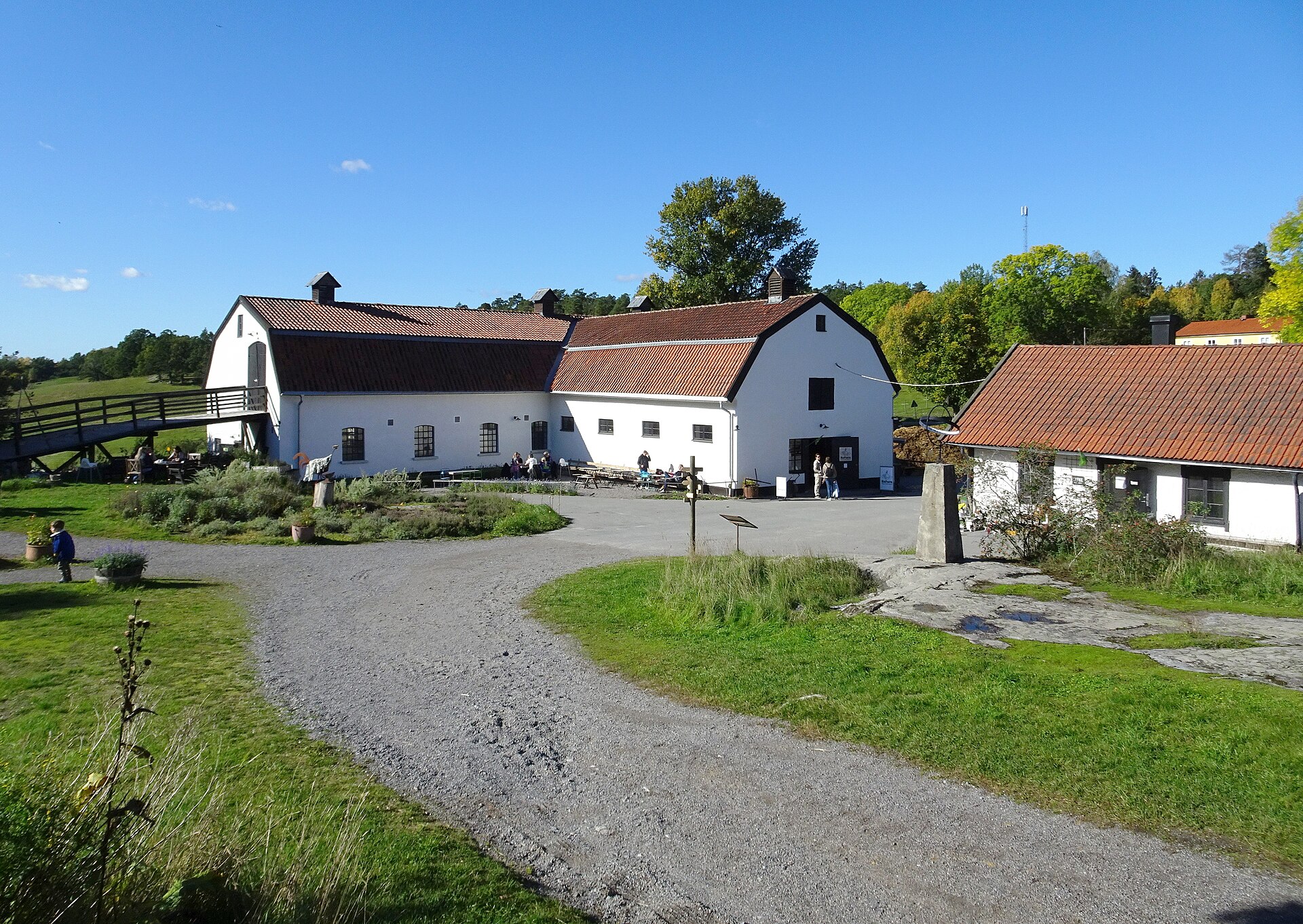 Gårdsplanen på Elfviks gård med vitkalkade ekonomibyggnader och besökare en solig höstdag