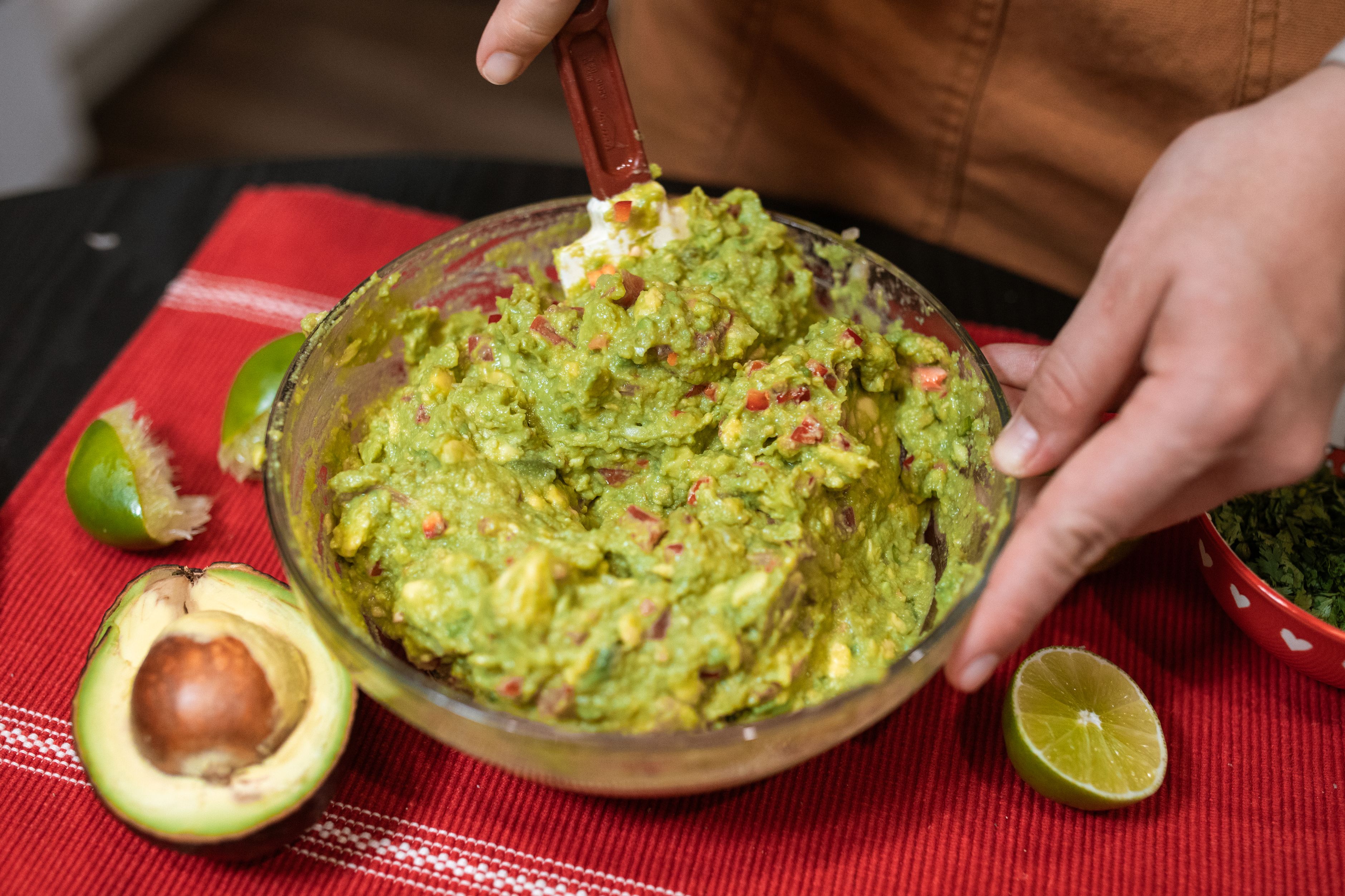 Krämig guacamole i skål med avokado, lime och tomat, mixas med gaffel