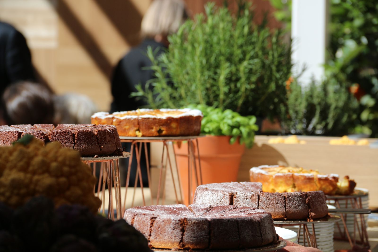 Tårtbord utomhus med flera hela kakor på fat, uppskurna i bitar och pudrade med florsocker