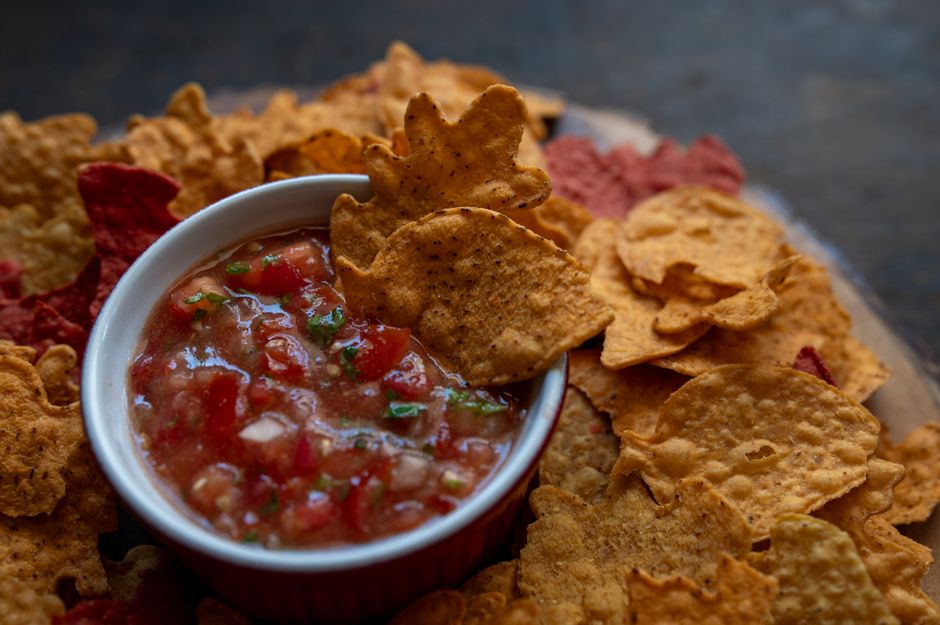 Skål med rödfärgad salsa av tomat, lök och koriander omgiven av tortillachips