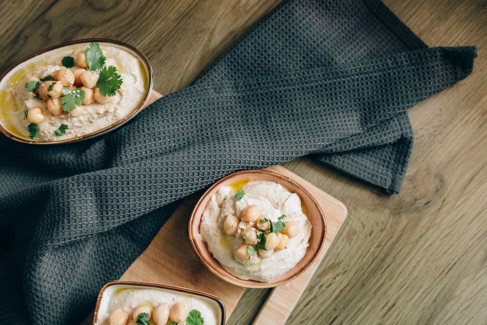 Tre skålar med krämig hummus toppad med hela kikärtor, koriander och olivolja
