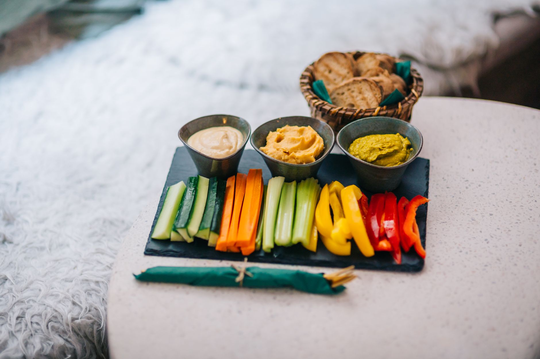 Grönsaksstavar av gurka, morot, selleri och paprika på skifferbricka med tre dippar och kex
