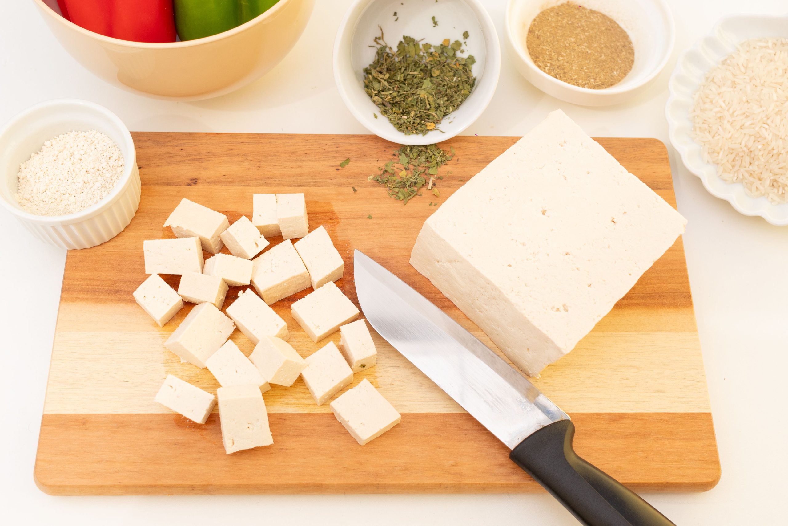 Fast tofu skärs i bitar på skärbräda bredvid skålar med kryddor