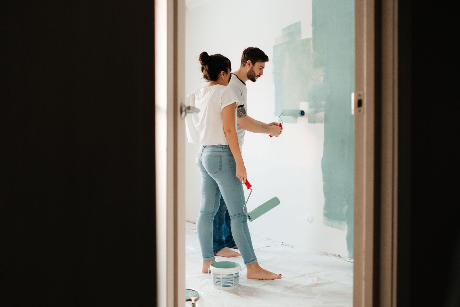 Ett par målar en vägg med roller under en sommarrenovering