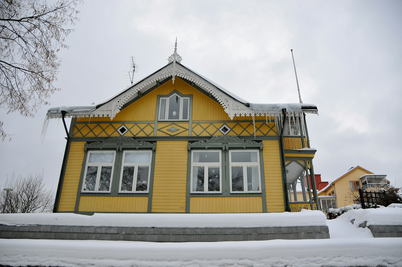 Gult trähus med snö på taket och istappar längs takfoten.