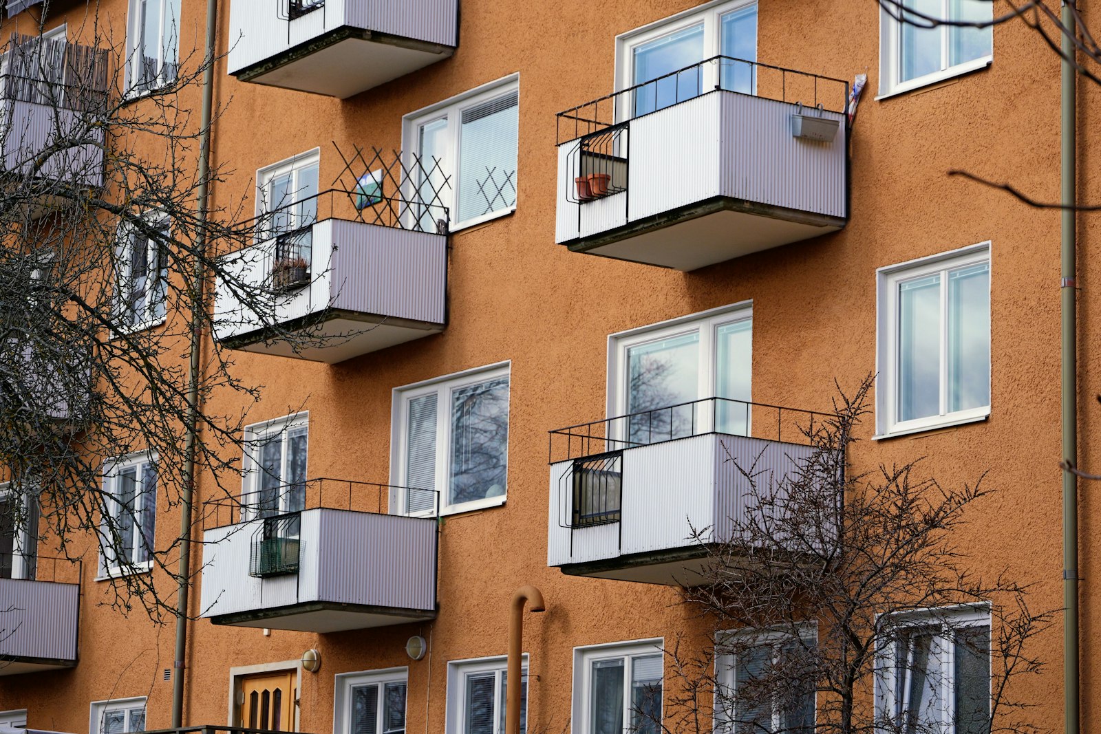 Små utkragande balkonger med vita plåtfronter på ett orange putsat flerbostadshus en tidig vår.