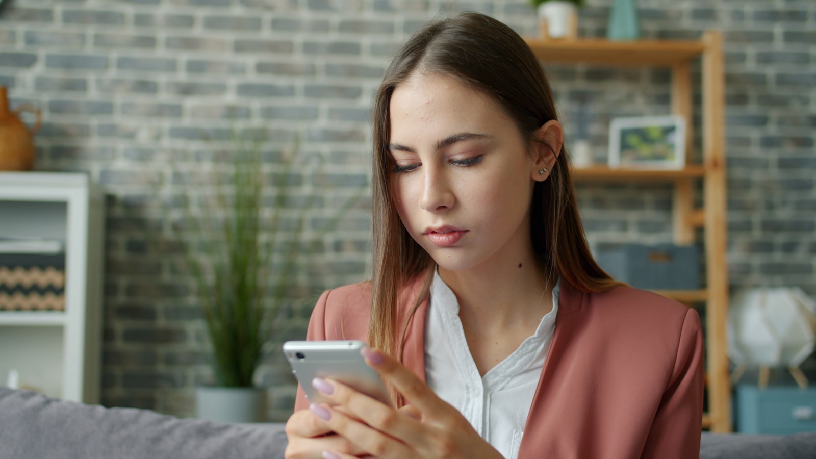 Kvinna sitter i en soffa och granskar uppmärksamt ett meddelande på sin mobiltelefon
