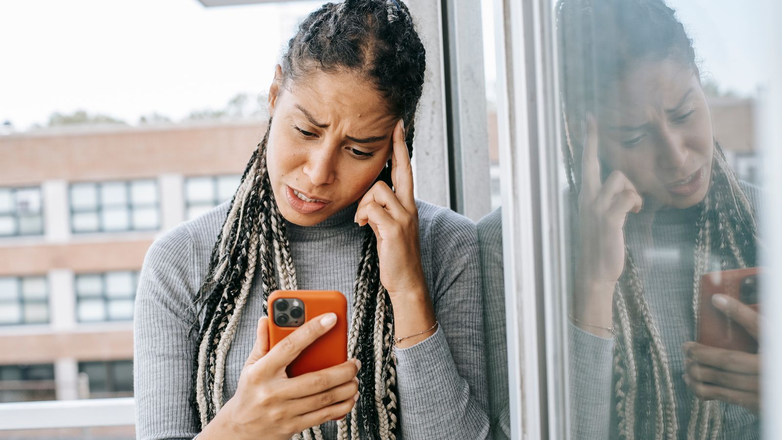 Kvinna tittar bekymrat på sin mobiltelefon vid ett fönster