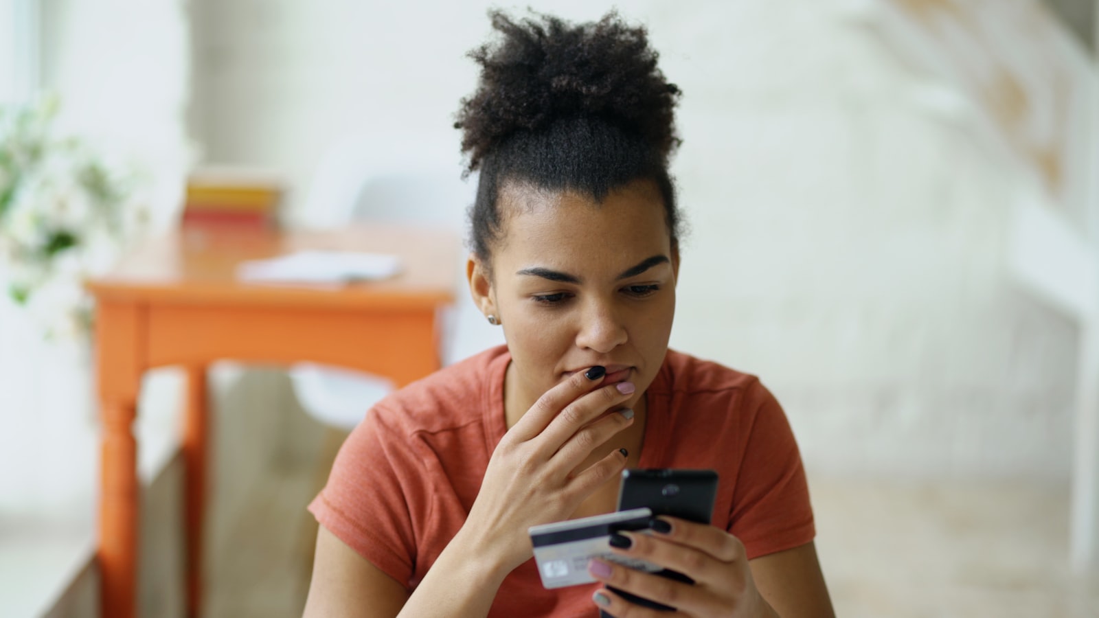 Kvinna tittar bekymrat på sin mobiltelefon med ett betalkort i handen