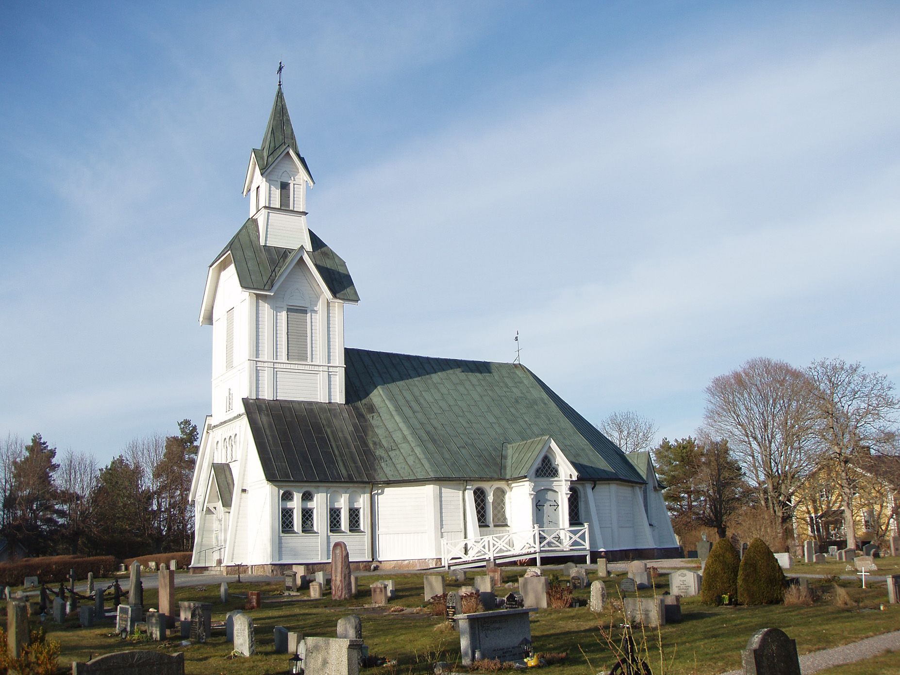Ljusterö kyrka sedd utifrån, vitmålad träkyrka med grönt tak och spira, omgiven av kyrkogård