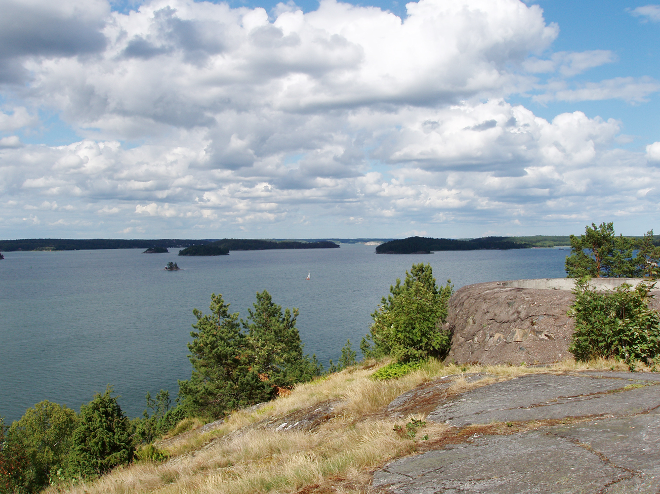 Utsikt från berghällen på Ljusterö huvud över fjärden och skogklädda öar, med resterna av ett betongfundament till höger